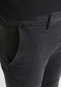 Black denim jeans with a smooth texture, featuring side pockets and a classic fit. Stitched detailing along the waistband and pockets.
