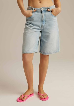 Jasnoniebieskie szorty dżinsowe o luźnym kroju, z kieszeniami z przodu i zapięciem na guziki. Połączone z jaskraworóżowymi klapkami.