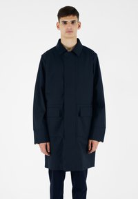 Cappotto lungo blu navy con colletto, due tasche frontali e taglio dritto. Presenta una texture liscia e una chiusura frontale nascosta.