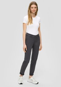 Pantaloni grigio chiaro a sigaretta con orli arrotolati, realizzati in una morbida miscela di cotone, dotati di tasche frontali e design piatto davanti. Indossati con una maglietta bianca e sneakers.