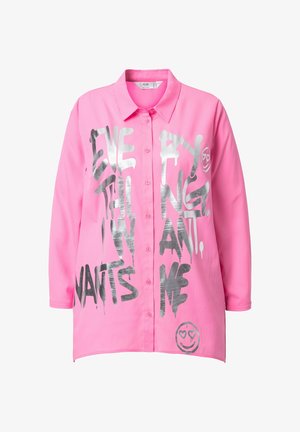 Camisa de botones rosa con mangas largas, que presenta un gran texto plateado y un gráfico de una carita sonriente con ojos de corazón. Tela suave y corte relajado.