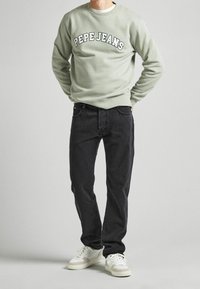 Ljusgrön sweatshirt med "PEPE JEANS" tryck, kombinerad med mörka jeans och vita sneakers. Enkelt designad med rund hals och avslappnad passform.