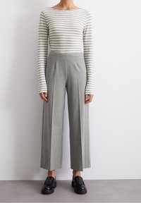 Gestreiftes Langarmoberteil in Hellgrau und Weiß, kombiniert mit hoch taillierten grauen weiten Hosen. Schwarze Slipper runden das Outfit ab.