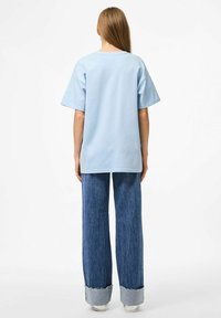 Gaiši zils pārāk liels T-krekls ar īsām piedurknēm, kopā ar platu kāju džinsiem ar plīsu malu. Vienkāršs dizains, vienkrāsains.