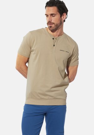 Beige short-sleeve shirt with a rounded neckline, two-button placket, and dark green logo text. Smooth cotton blend fabric and relaxed fit.