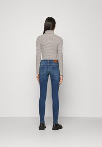Camiseta de rayas de manga larga con cuello alto y jeans ajustados azules. Los jeans tienen un parche de cuero marrón en la cinturilla y un diseño ceñido.