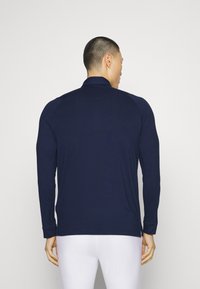 Long-sleeve navy shirt made of a smooth, stretchy fabric with a zip collar, featuring flat seams and side slits at the hem.