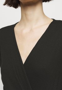 Top avvolgente nero a coste con scollatura a V profonda, che mette in mostra una texture morbida e una leggera lucentezza, perfetto da indossare a strati o come capo indipendente.