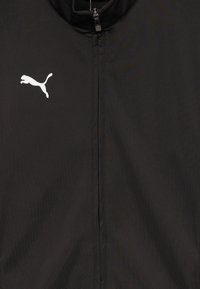 Chaqueta negra de tela suave, con un cuello alto y una cremallera en la parte delantera. Logo de Puma en blanco mostrado de manera destacada en el lado izquierdo.