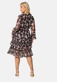 Svart blommig klänning med genomskinliga, volangärmar och trelagers kjol. Har rosa och vita blommönster, kompletterad med nakna klackar.