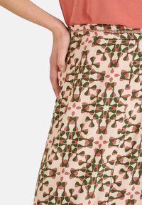 Falda estampada con un fondo claro decorado con formas y acentos geométricos en verde y rosa. El material parece ligero y suave.