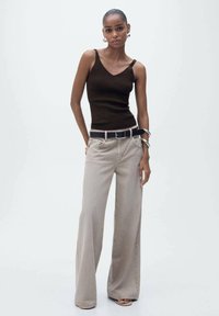 Top tank fitted marrone, jeans a gamba larga beige chiaro, vita con cinturino nera e accessori argentati. Texture liscia, design minimalista, colori neutri.
