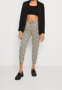 Czarno-białe wzorzyste spodnie cropped z geometrycznymi motywami, połączone z dopasowanym czarnym topem cropped i czarnym żakietem. Czarne mokasyny.