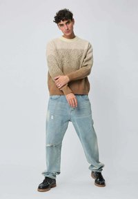 Pull en tricot avec dégradé beige et marron, col rond ; associé à un jean bleu clair déchiré et des chaussures à lacets noires.