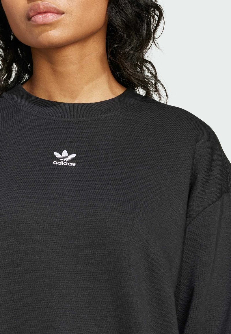 Sort sweatshirt med ribbet rund hals, der har en lille hvid Adidas-logo brodering på brystet; glat tekstur og afslappet pasform.