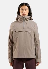 Beige wasserfeste Jacke mit hohem Kragen, Reißverschluss und Fronttasche; verfügt über eine verstellbare Kapuze und verstellbare Bündchen; glatte Textur.
