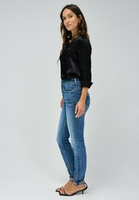 Vaqueros de denim azul con un corte ajustado, deslavados en los muslos y dobladillos enrollados. Combinados con una blusa negra, abotonada, de manga larga y sandalias de tacón negras.