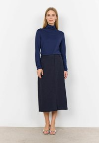 Navyblauer Rollkragenpullover kombiniert mit einem dunkel gestreiften Midirock. Das Outfit hat eine figurbetonte Silhouette und elegante Sandalen.