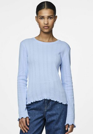 Blå ribbad långärmad topp med scalloped fåll och strukturerat mönster, kombinerad med mörka denimjeans. Mjuk stickad tyg.