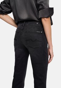 Svarta denimjeans med en figurnära passform, med bakfickor och subtila sömnadsdetaljer. Materialet har en slät textur.