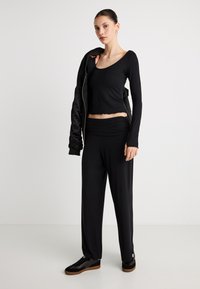 Μαύρο μακρυμάνικο τοπ με κυματιστό τελείωμα, σε συνδυασμό με άνετο μαύρο παντελόνι. Και τα δύο είναι από μαλακό ύφασμα, συμπληρωμένα με μαύρα αθλητικά παπούτσια.