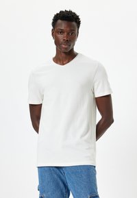 Witte T-shirt met korte mouwen en een V-hals, gemaakt van zachte stof, gecombineerd met blauwe denim jeans. Eenvoudig ontwerp, geen zichtbare patronen of accenten.