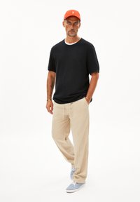 Männeroutfit mit einem dunkelblauen kurzärmligen Pullover, beigen Hosen und hellblauen Sneakers. Eine orange Kappe rundet das Outfit ab.