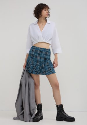 Gekürzte weiße Bluse, türkis karierten Minirock mit Rüsche, grauer Blazer locker drapiert, schwarze Schnürkampfstiefel. Einfaches Design und klare Linien.