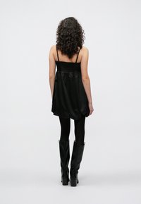 Μαύρο αμάνικο φόρεμα με σφηκοφωλιά στ�ο μπούστο και ροή φούστα, συνδυασμένο με μαύρες καλσόν και μπότες με τακούνι έως το γόνατο. Ορατά μπούκλα μαλλιών.