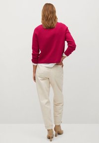 Fuchsia gekürzter Pullover kombiniert mit hellbeigen, hochgeschnittenen Hosen und nudefarbenen, hochhackigen Schuhen. Weicher Stoff und lässige Passform.