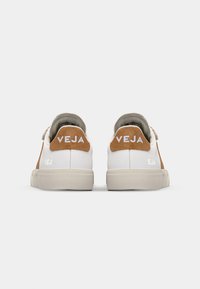 Hvite sneakers med brune semskede detaljer og en lys grå gummisåle. Har preget "VEJA" merkevare på hælen. Minimalistisk design.