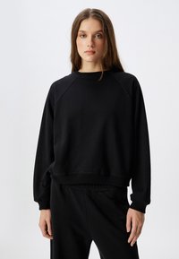 Zwarte sweatshirt met een ronde hals en raglanmouwen. Zacht materiaal, aansluitende tailleband en een minimalistisch ontwerp, gecombineerd met bijpassende zwarte broek.