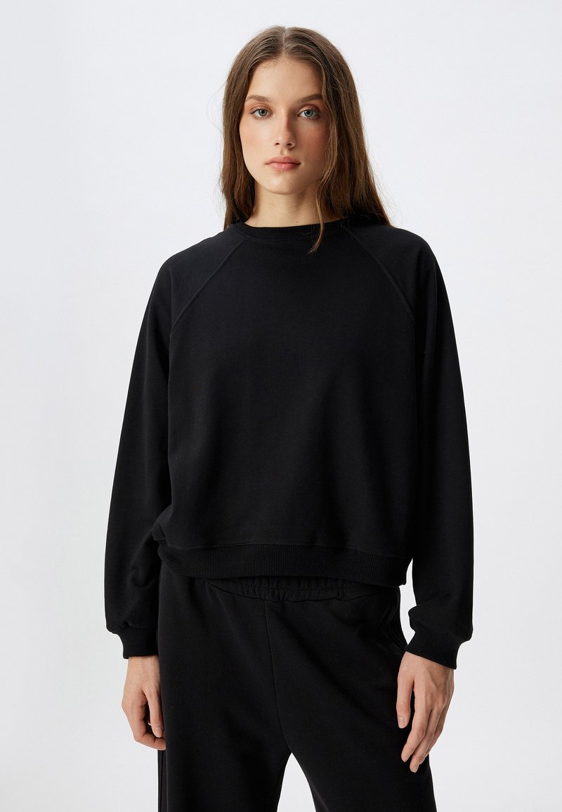 Zwarte sweatshirt met een ronde hals en raglanmouwen. Zacht materiaal, aansluitende tailleband en een minimalistisch ontwerp, gecombineerd met bijpassende zwarte broek.