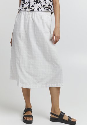 Jupe en lin blanche avec une taille élastique, longueur genou, dotée d'un tissu texturé. Accompagnée de sandales à plateforme noires sur un fond neutre.