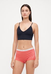 Crni pamučni bralette s tankim trakama u kombinaciji s koraljnim šortsevima koji imaju bijeli elastični pojas označen logotipom.