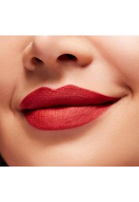 Rossetto rosso opaco su labbra lisce, evidenziando una forma ben definita con una morbida texture e lievi pieghe, su uno sfondo di un tono di pelle naturale.