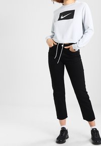 Světle modrý zkrácený svetr s černým logem Nike, černé zúžené kalhoty a černé tenisky. Svetr má detail s tkanicí.