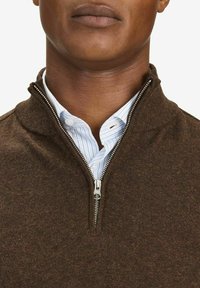 Brauner Strickpullover mit Reißverschlusskragen, über einem blau-weiß gestreiften Hemd getragen. Das Material scheint weich mit einer strukturierten Oberfläche zu sein.