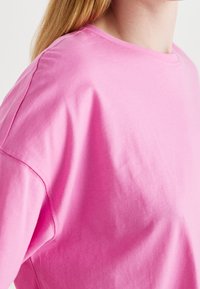 Růžové bavlněné tričko s krátkým rukávem, kulatým výstřihem a jemnou strukturou, s viditelným šitím a volným střihem.