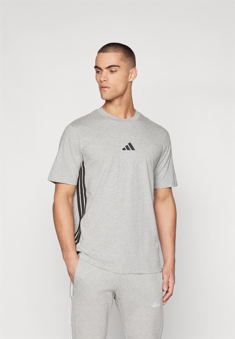 T-shirt gris à manches courtes avec logo Adidas noir et trois bandes noires sur les côtés, fabriqué dans un tissu lisse et respirant.