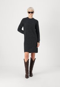 Σκουρόχρωμο γκρι πλεκτό φόρεμα με μακριά μανίκια, στρογγυλή λαιμόκοψη και πλαϊνές τσέπες, συνδυασμένο με καφέ καουμπόικες μπότες με διακοσμητική ραφή.