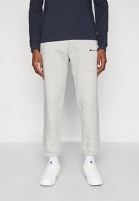 Ανοιχτό γκρι παντελόνι φόρμας με ελαστικά μανσέτες, με μικρό ναυτικό μπλε λογότυπο. Συνδυασμένο με λευκά αθλητικά παπούτσια και ναυτικό μπλε μακρυμάνικο πουκάμισο.