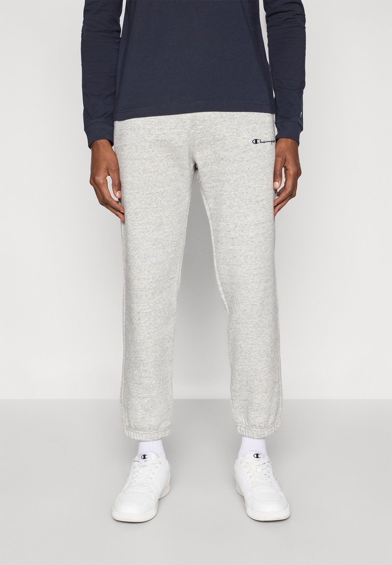 Ανοιχτό γκρι παντελόνι φόρμας με ελαστικά μανσέτες, με μικρό ναυτικό μπλε λογότυπο. Συνδυασμένο με λευκά αθλητικά παπούτσια και ναυτικό μπλε μακρυμάνικο πουκάμισο.