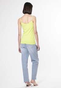 Top senza maniche giallo neon con spalline sottili, abbinato a jeans larghi blu chiaro con orlo sfilacciato e sandali con tacco bianchi.