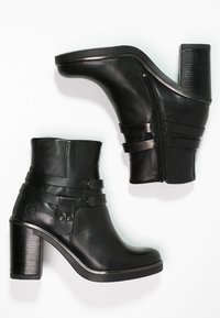 Botas de tobillo de cuero negro con tacón afilado, que presentan dos correas horizontales y un cierre lateral de cremallera. Textura suave y detalles de acento geométricos.