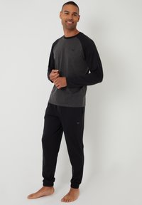 Camiseta de manga larga gris con mangas raglán negras, combinada con pantalones de chándal negros con puños elásticos y un pequeño logo en el lateral.