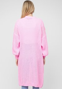 Cardigan lungo di un leggero rosa pallido, con maniche ampie, schiena aperta e tessuto strutturato. Adatto per essere indossato a strati sopra diversi outfit.