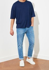 T-shirt bleu marine oversize, coupe décontractée, associée à un jean slim bleu clair. Des baskets blanches à surface texturée complètent le look.