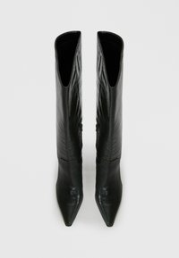 Bottes noires en cuir montantes avec un bout pointu, texture lisse et silhouette effilée, présentant une ouverture angulaire unique en haut.