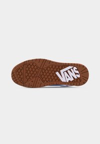 Semelle en caoutchouc marron d'une chaussure avec un motif en forme de gaufre et un logo Vans blanc sur un fond gris clair.